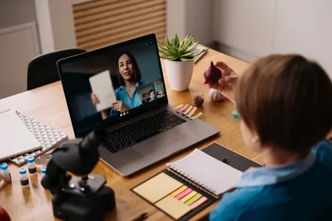 A teacher in Pakistan transitioning from traditional classroom teaching to online teaching, using a laptop and video conferencing tools to connect with students remotely.